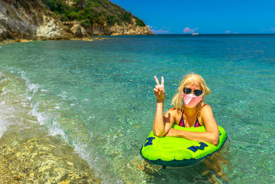 Portrait of woman wearing flu mask gesturing while swimming in sea