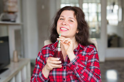 Happy woman holding juice in electric bulb at home