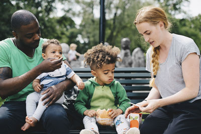 Parents having food with children while sitting on bench at park