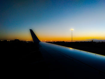 Airplane on airport runway against clear sky at sunset