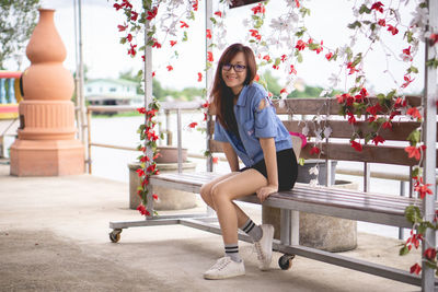 Portrait of smiling woman sitting on bench by floral decorations