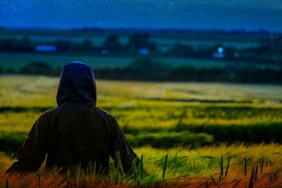 Rear view of man wearing hood clothing while sitting on field