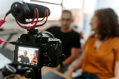 Professional camera with microphone on tripod recording video with unrecognizable man and woman during interview in studio