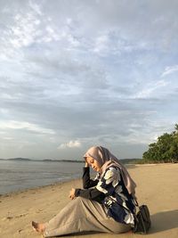 Woman sitting at beach against sky