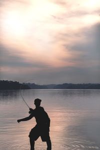 Rear view of silhouette man fishing in lake during sunset