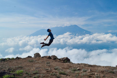 Hiker jumping on mountain peak against sky
