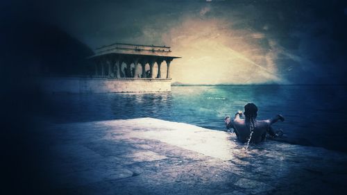 People sitting on bridge over sea against sky