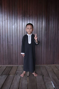 Portrait of boy standing against wooden wall