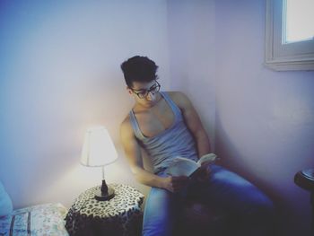 Young man reading book while sitting against wall at home