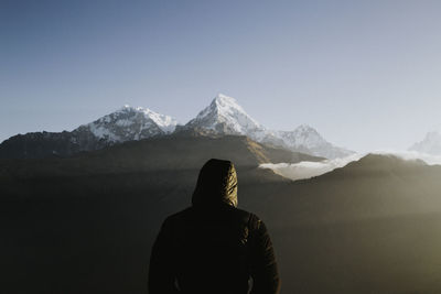 Rear view of man looking at snowcapped mountain against sky