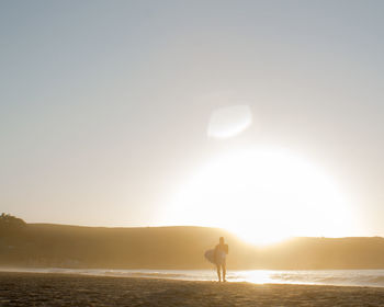 Silhouette man carrying surfboard at beach during sunset