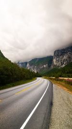 Empty road amidst mountains against cloudy sky