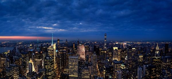 Illuminated buildings in city against cloudy sky