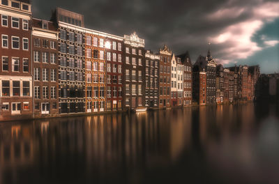 Illuminated buildings by river against sky in city