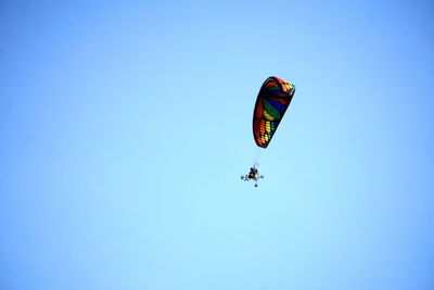 Low angle view of people paragliding against clear blue sky