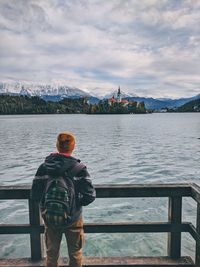Rear view of man standing by lake bled against sky.