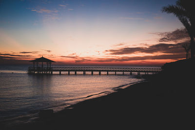 Silhouette pier over sea against sky during sunset