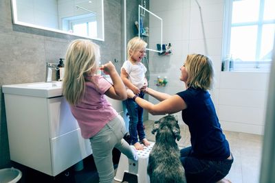 Smiling mother bonding while kneeling in bathroom by dog at home