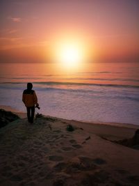 Rear view of man walking at beach during sunset