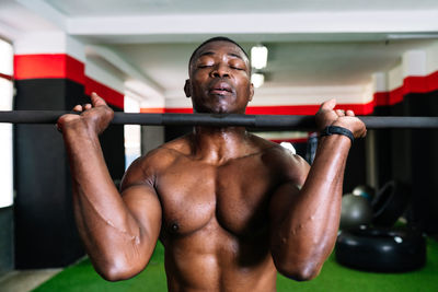 Strong african american male bodybuilder with muscular torso lifting heavy barbell during training in modern sports center