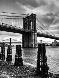 Suspension bridge over river against cloudy sky
