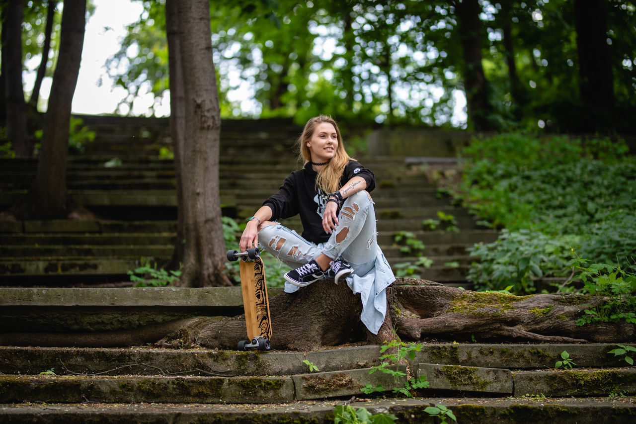 FULL LENGTH PORTRAIT OF SMILING YOUNG WOMAN SITTING ON LAND