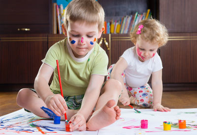 Cute kids painting on paper while sitting at home
