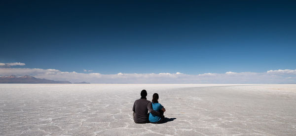 Couple sitting on desert against blue sky