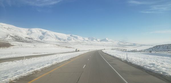 Road leading towards snowcapped mountains against sky