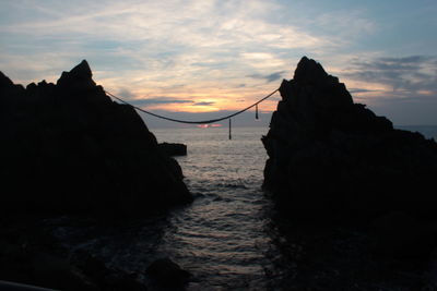 Silhouette rocks on sea against sky during sunset