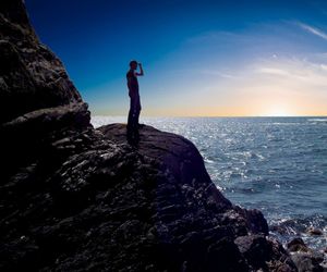 A man standing on rock by sea against sky