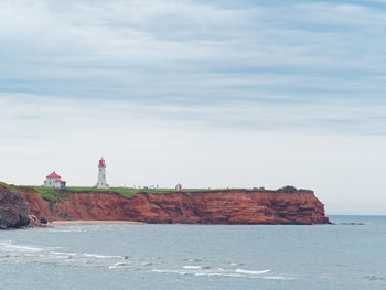 Lighthouse on rocks by sea against sky