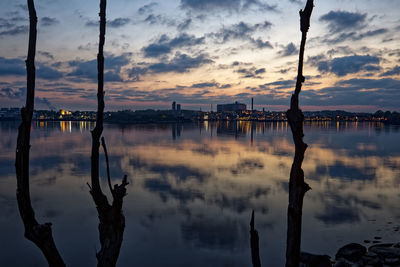Silhouette wooden posts in lake against sky during sunset