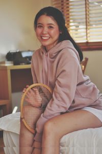 Portrait of smiling woman sitting on bed at home