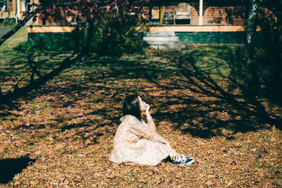 Side view of mid adult woman looking away while sitting on field in park during autumn