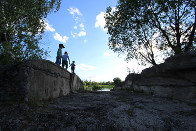 Children walking on retaining wall by footpath against sky