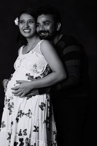 Smiling man touching belly of pregnant woman against black background