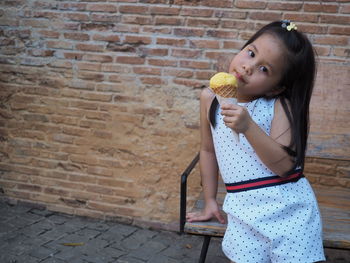 Portrait of girl holding ice cream against brick wall