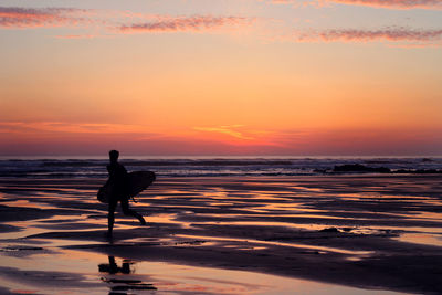 Silhouette man with surfboard on beach against sky during sunset