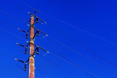 Low angle view of electricity pylon against clear blue sky