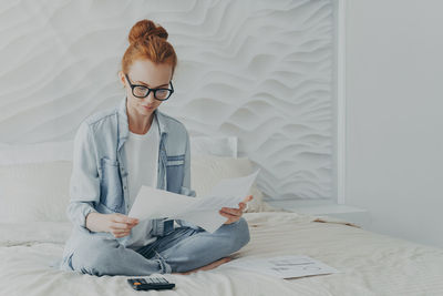 Young woman sitting on bed at home