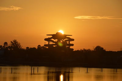 Scenic view of silhouetted water rides and trees with lake in foreground