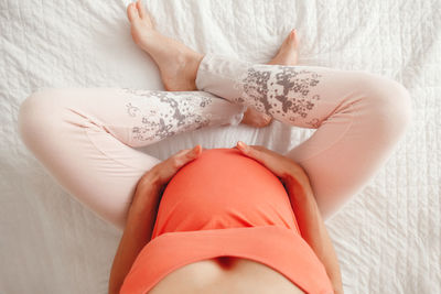 Low section of pregnant woman sitting on bed at home