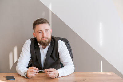Casual business man bearded, sitting at table with pen in his hand, thinking