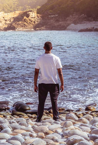 Rear view of man standing on rock at sea shore