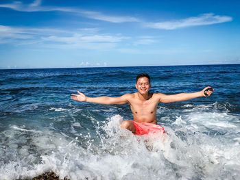 Portrait of shirtless man with arms outstretched in sea against sky during sunny day