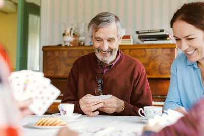 Happy senior man playing cards with family at home