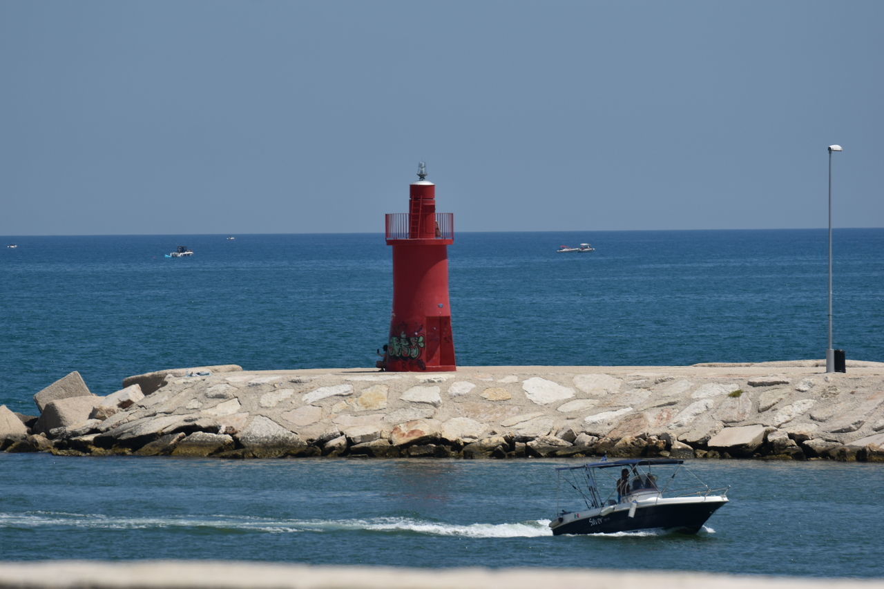 lighthouse, water, sea, guidance, tower, sky, security, architecture, protection, coast, nautical vessel, transportation, ocean, built structure, nature, building exterior, beach, breakwater, building, horizon over water, horizon, clear sky, land, shore, vehicle, scenics - nature, no people, day, mode of transportation, travel destinations, travel, coastline, outdoors, blue, beauty in nature, bay, motion, navigational equipment, nautical equipment, channel, rock, tranquility, tranquil scene