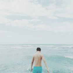 Rear view of shirtless man in sea against sky