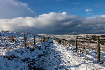 Snow covered wooden posts on field against sky